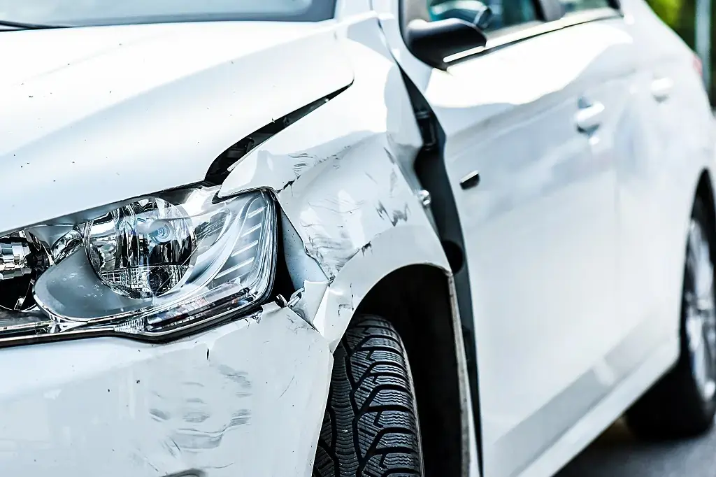 A silver Volkswagen Tiguan SUV with severe front left damage, including a smashed headlight, crumpled fender, and flat tire, parked on a street with debris.