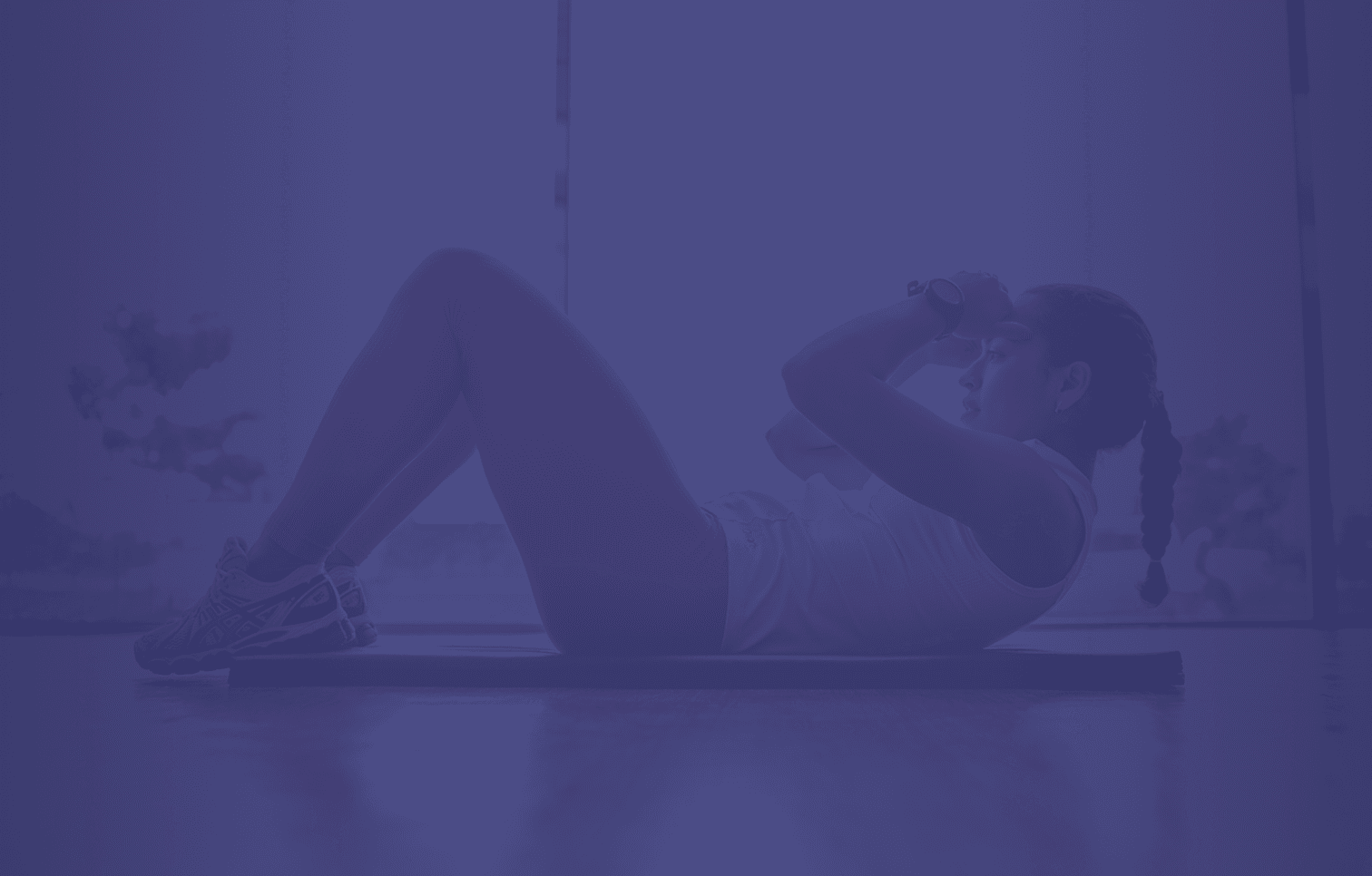 A woman with braided hair wearing athletic clothing and a smartwatch is performing crunches on a mat indoors.