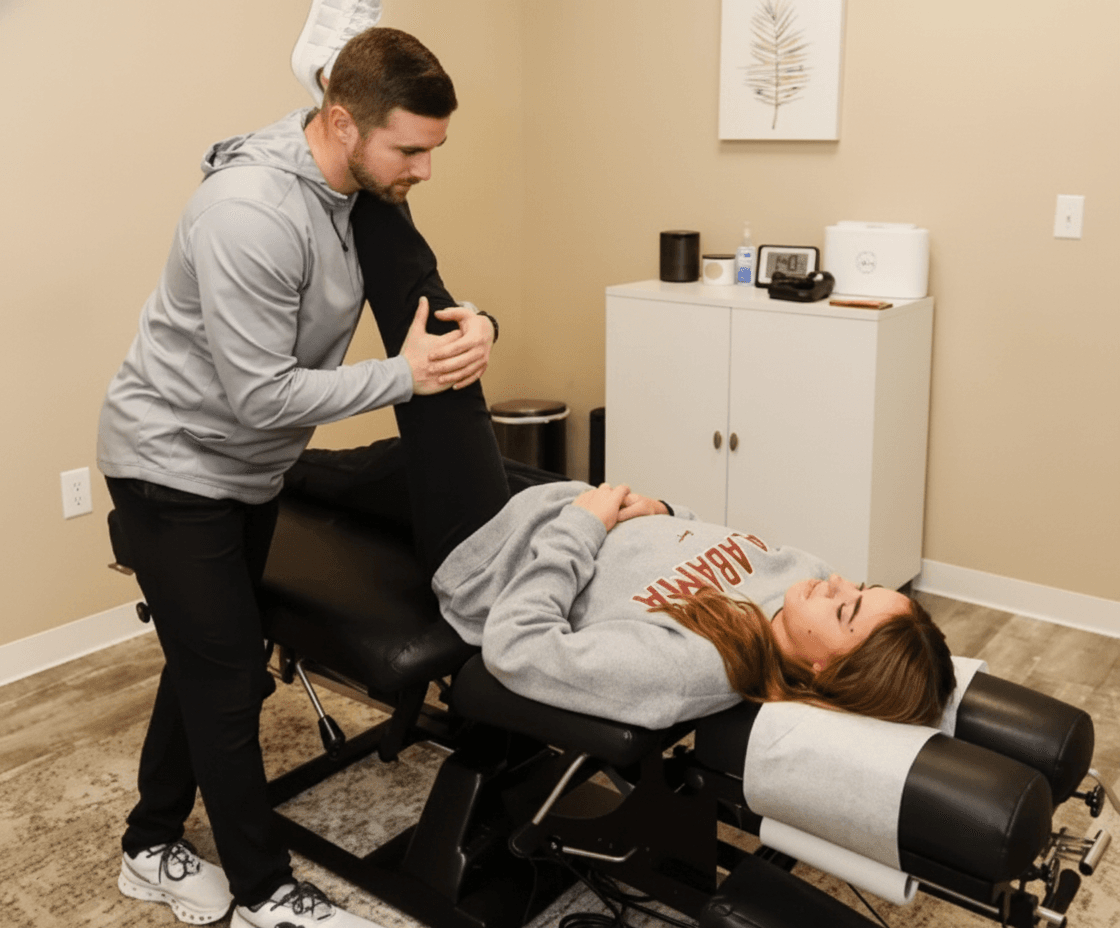 A male chiropractor stretches a female patient's leg on a treatment table in a modern clinic.